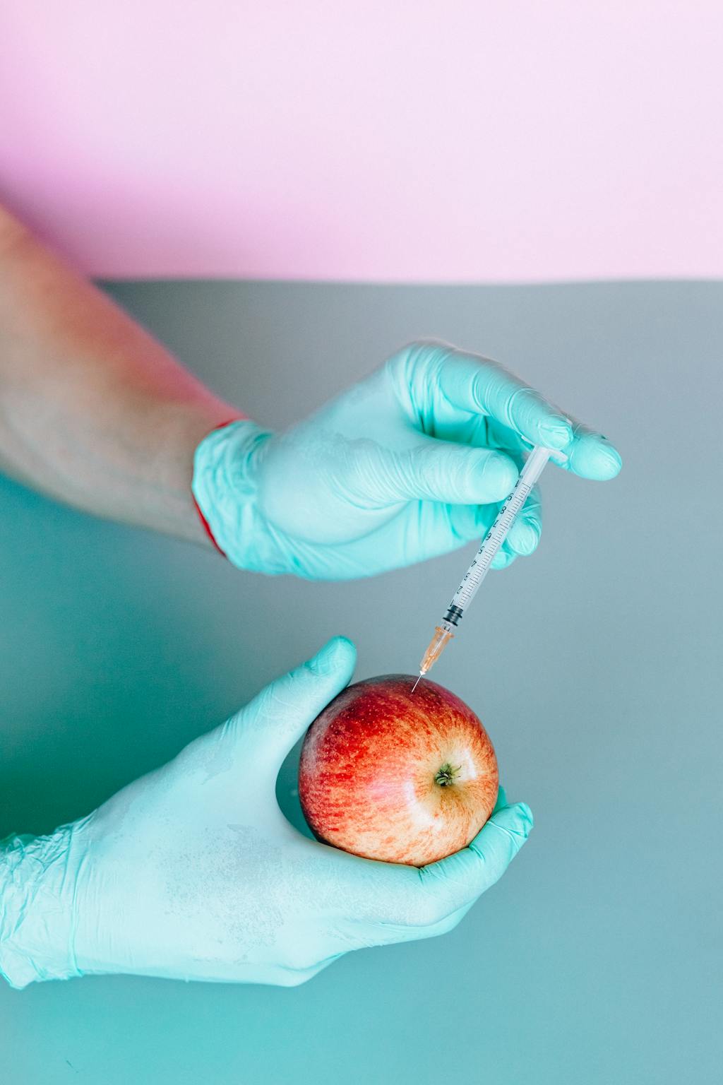 Person with gloves injecting apple, symbolizing healthcare experimentation.
