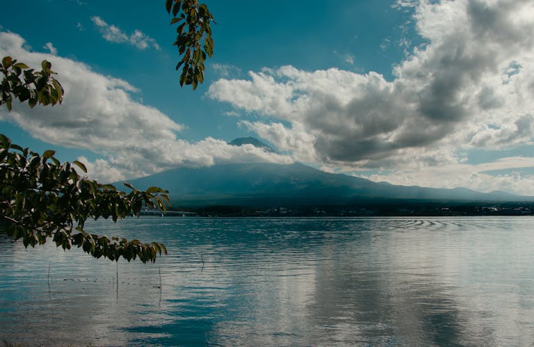 Beautiful lake reflecting mountains and clouds with lush foliage framing the scene.